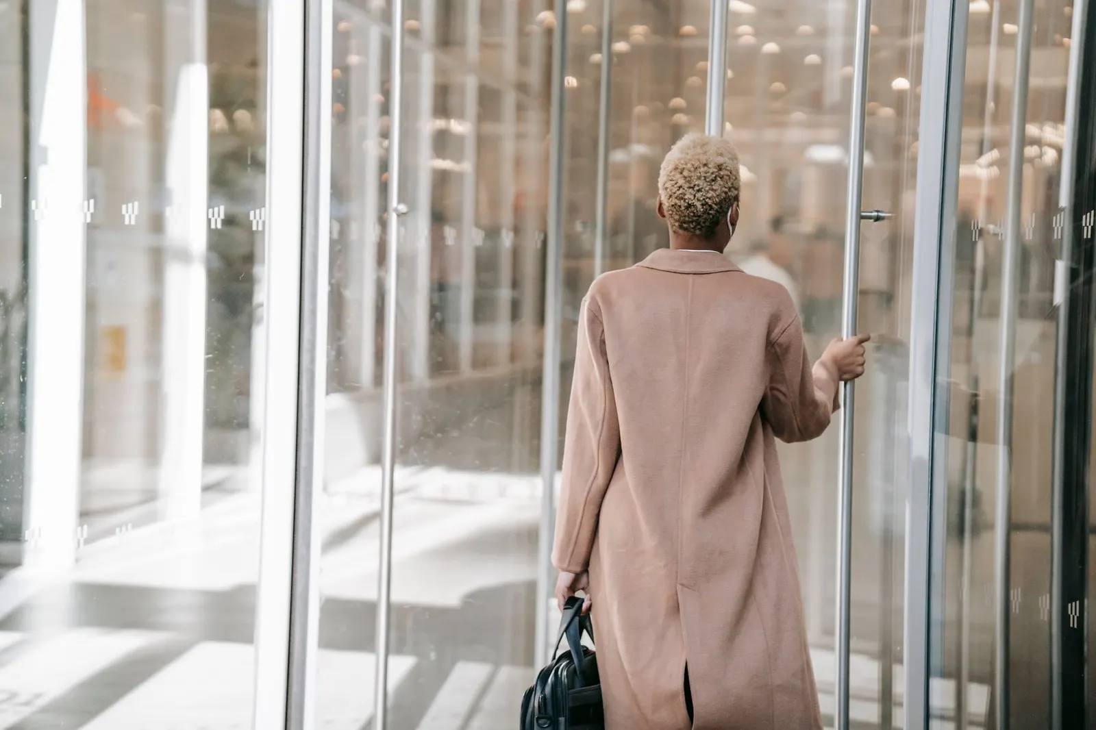 A professional walking through the glass entrance doors of a modern office